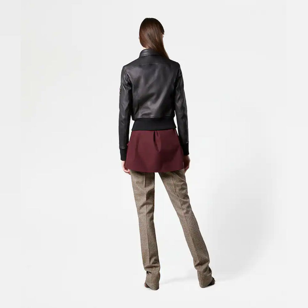 Person wearing a black leather jacket, burgundy top, and beige pants on a white background