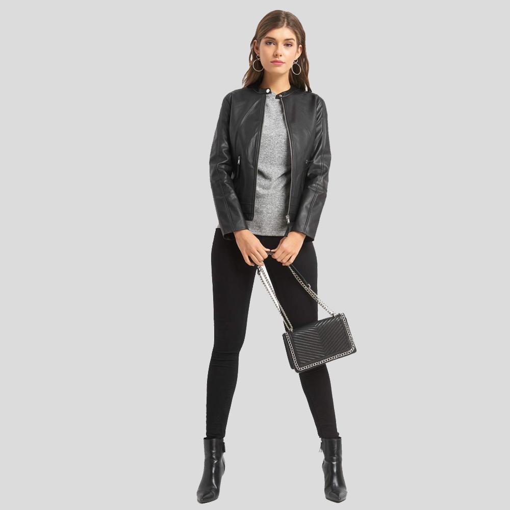 Woman wearing a black leather jacket, gray shirt, black pants, and black boots, holding a black handbag on a light gray background.