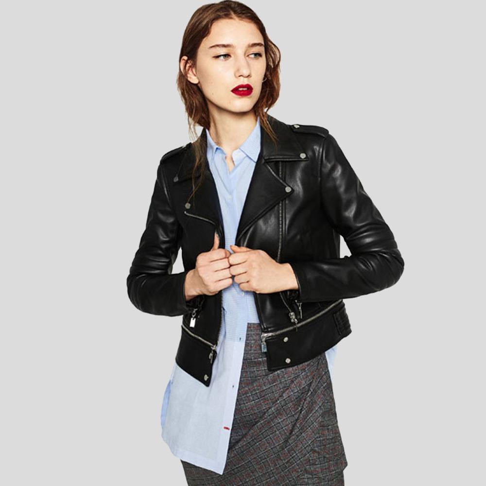 Woman wearing a black leather jacket over a light blue shirt and gray skirt on a plain background
