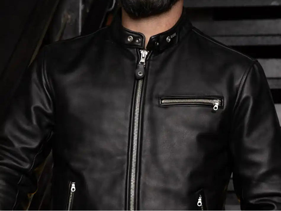 A close-up of a man wearing a black leather motorcycle jacket with a mandarin collar, silver zippers, and a zippered chest pocket.