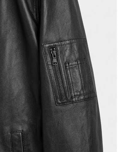 Close-up of a black leather jacket sleeve showing a zippered pocket on the upper arm against a light gray background.