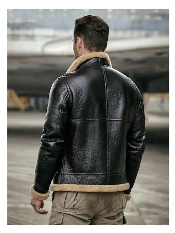 Man wearing a black leather jacket with beige fur lining, standing in an industrial setting.
