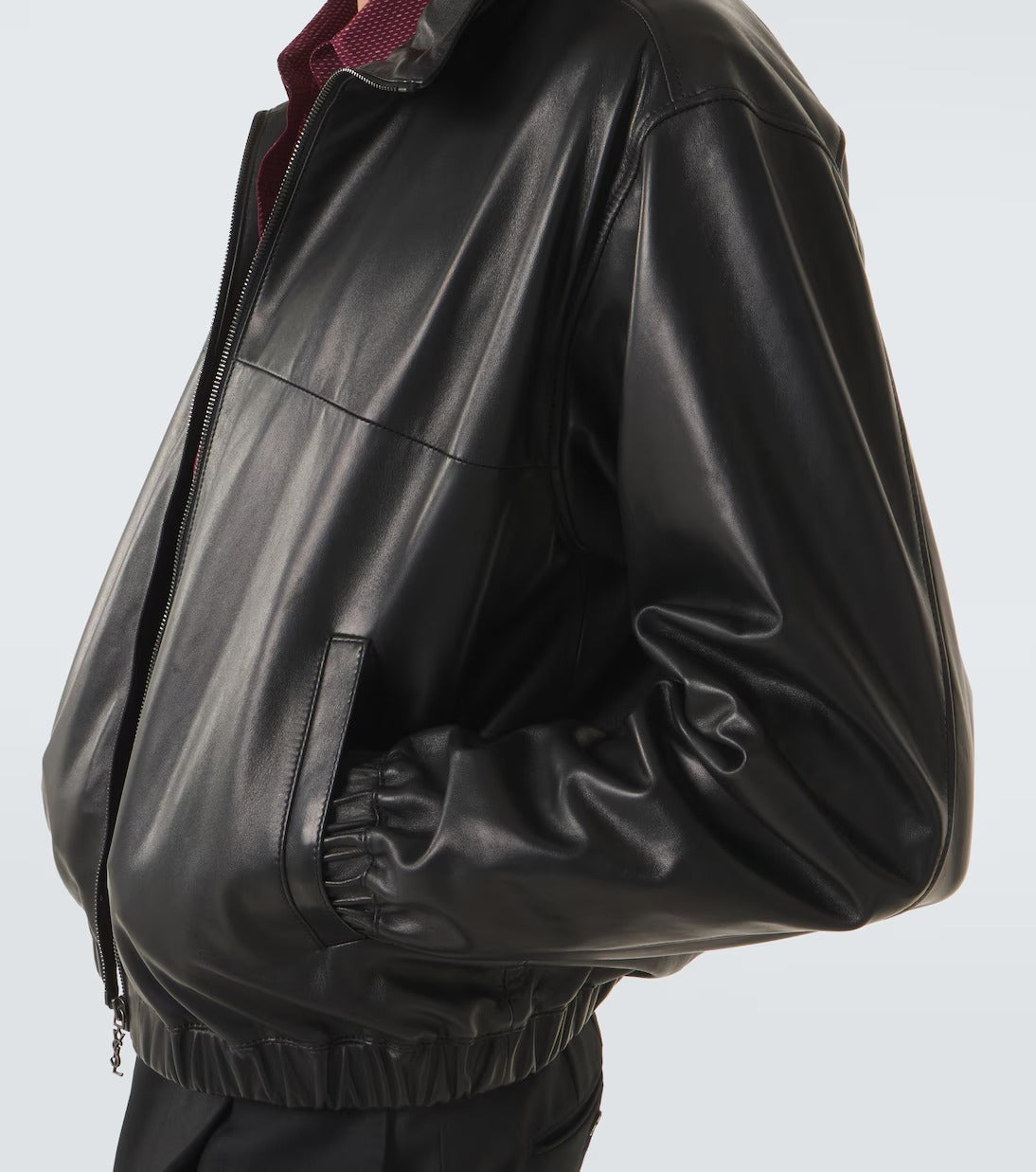 A close-up side view of a person wearing a black leather jacket over a dark burgundy collared shirt, against a light gray studio background.