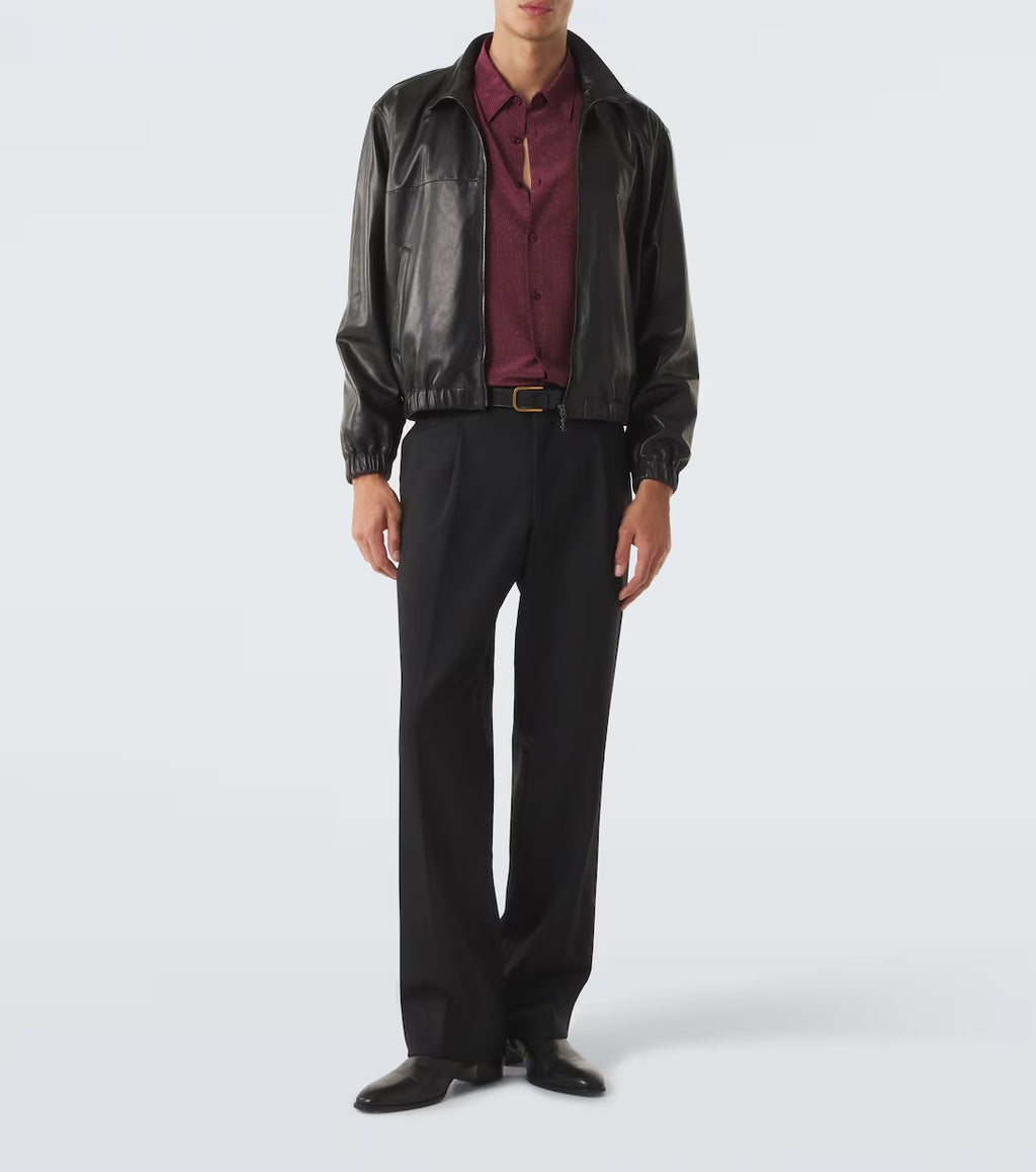 A model wearing a black leather jacket, a burgundy button-down shirt, black trousers, and black leather shoes, standing against a light gray studio background.