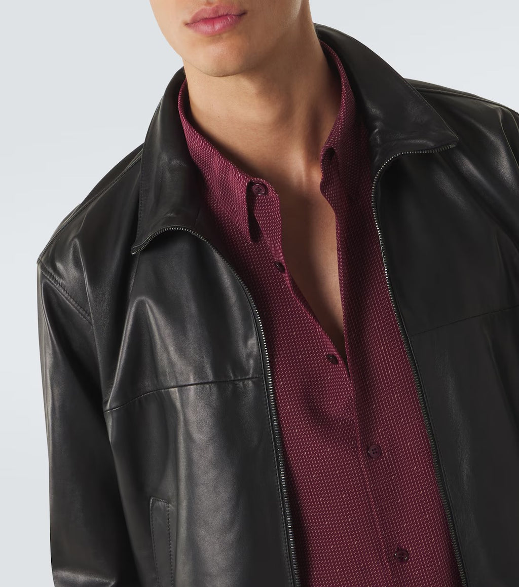 A close-up of a person wearing a black leather jacket over a burgundy textured button-up shirt, cropped from the lower face to the upper torso against a light gray studio background.