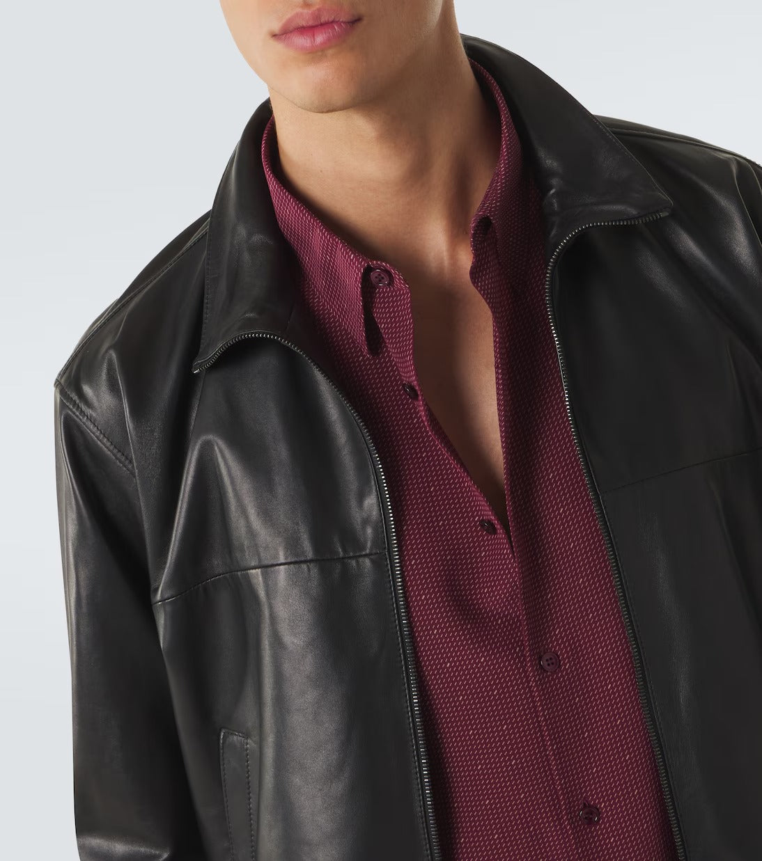 A close-up of a person wearing a black leather jacket over a burgundy textured button-up shirt, cropped from the lower face to the upper torso against a light gray studio background.