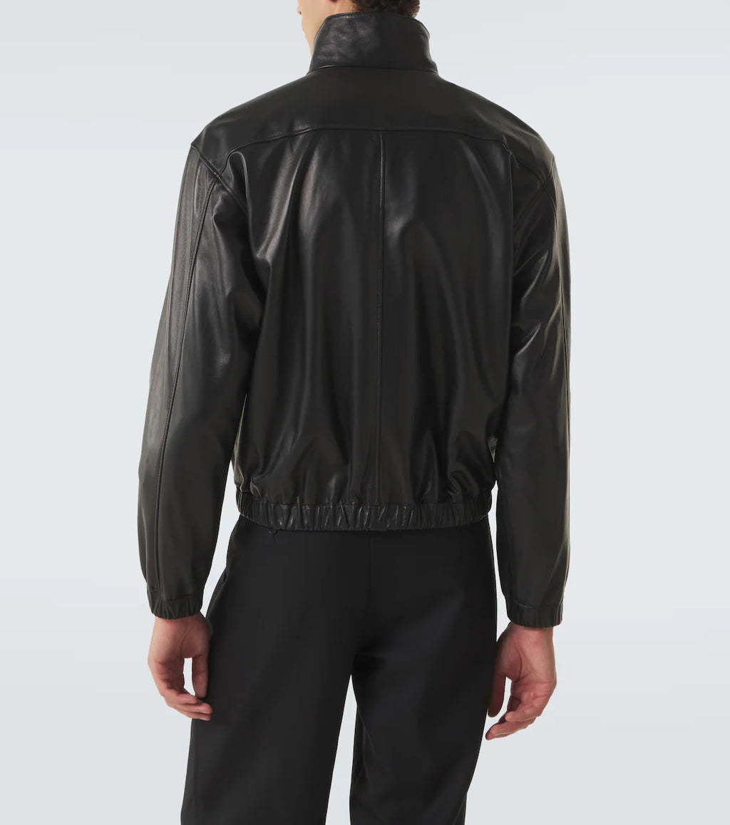 A person shown from the back wearing a black leather jacket with a high collar and elastic hem, paired with black pants, against a light gray studio background.