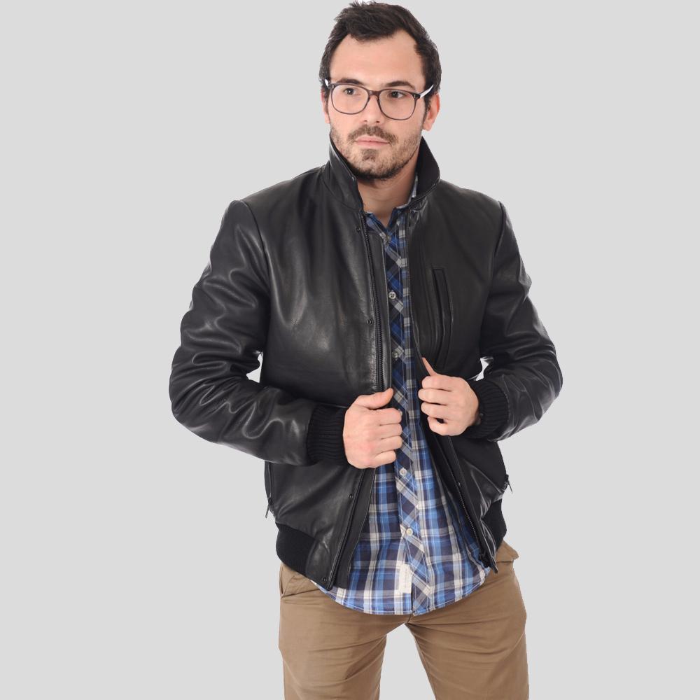 Man wearing a black leather jacket over a plaid shirt on a light gray background