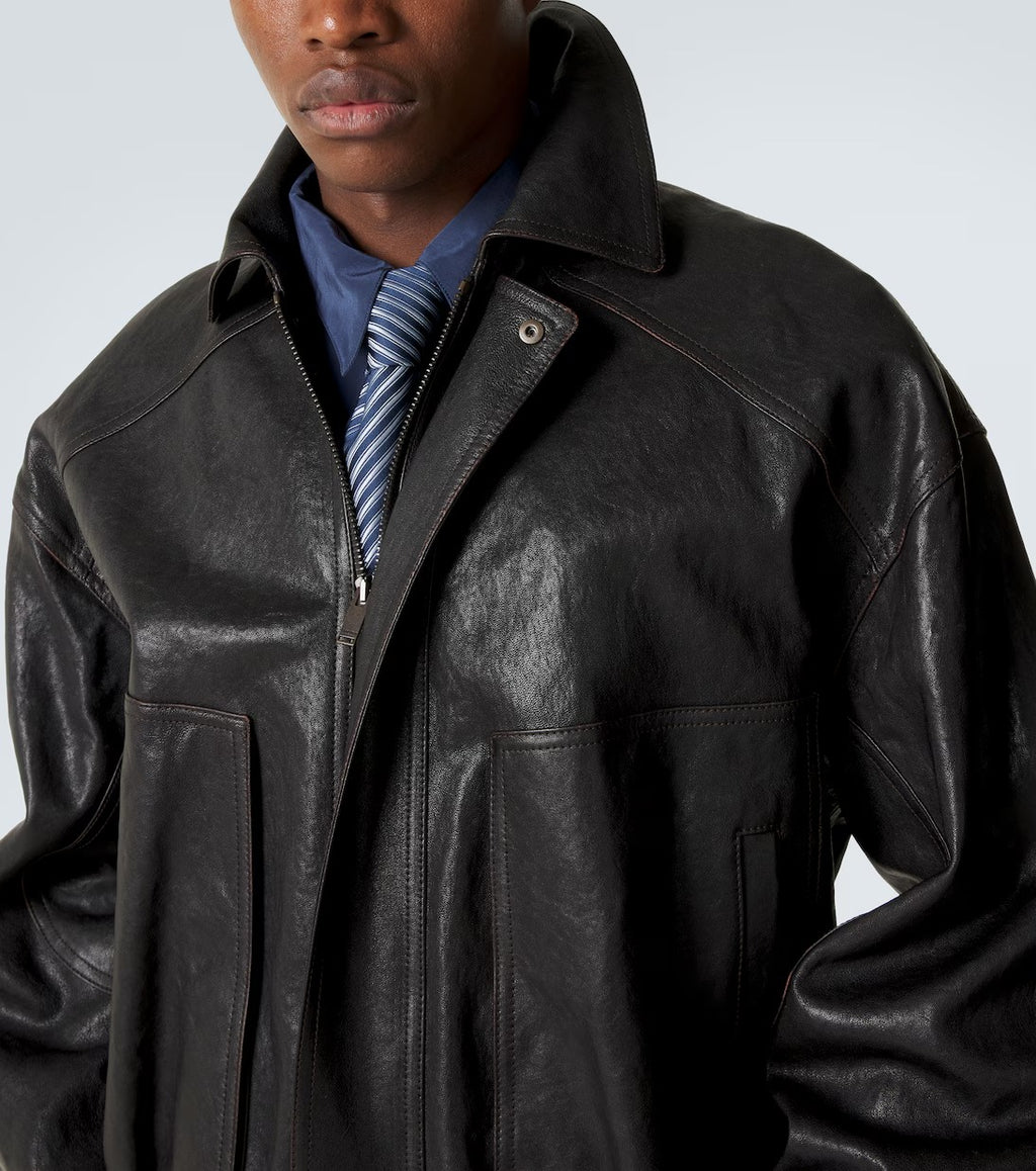 Man wearing a black leather jacket over a blue shirt with a striped tie against a light gray background