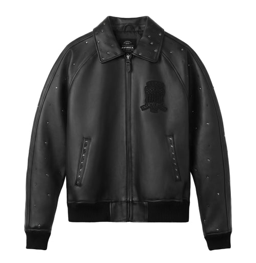 A black leather bomber jacket with silver studded details, a black embroidered skull patch on the left chest, and a front zipper, shown against a plain white background.