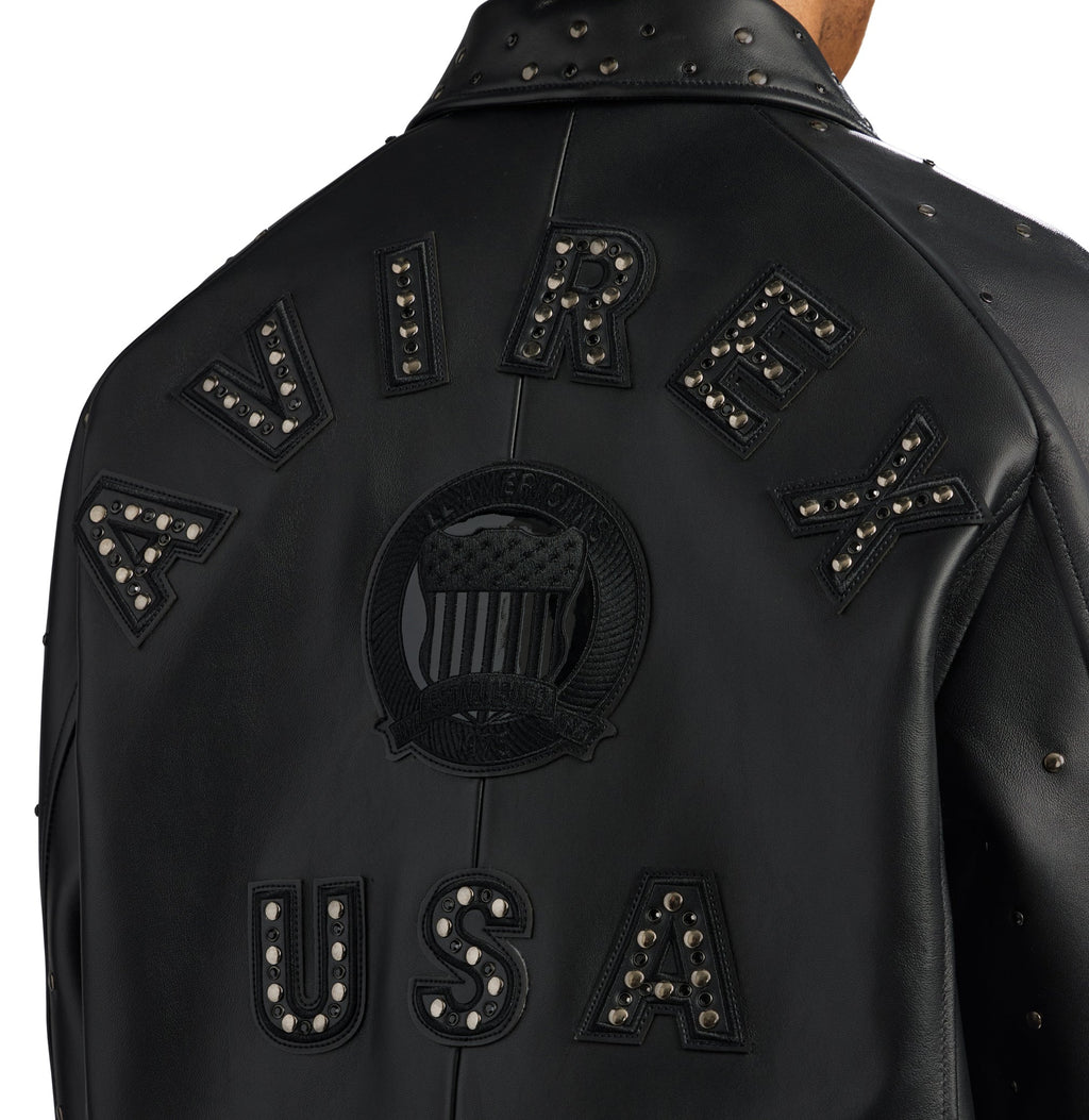 Close-up back view of a black leather jacket with studded lettering reading 'AVIREX' and 'USA' on a white background.