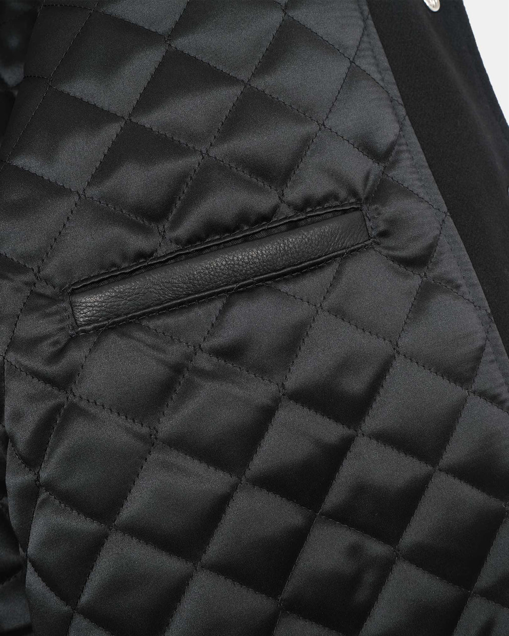 Close-up of a black quilted jacket with a diamond patterned fabric and a horizontal leather trim detail.