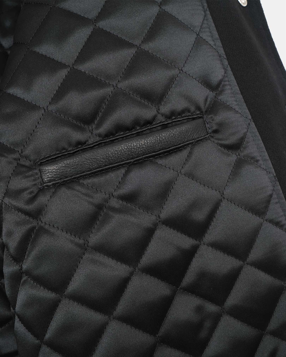 Close-up of a black quilted jacket with a diamond patterned fabric and a horizontal leather trim detail.