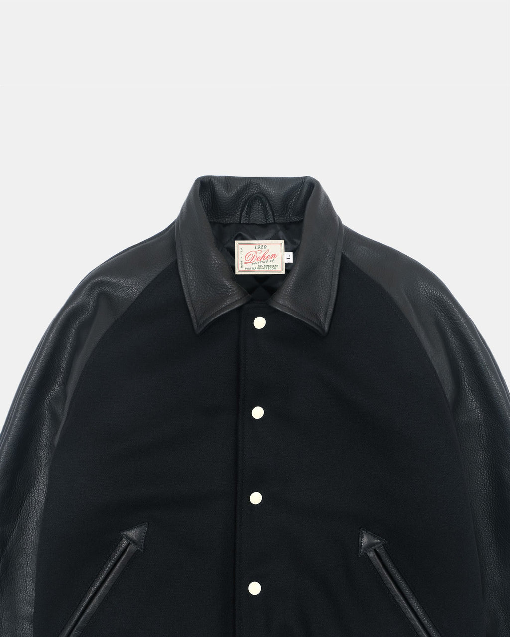 A close-up of a black jacket with contrasting dark brown leather-like collar, shoulders, and front zipper details, featuring white snap buttons and a visible 'Klim' brand label.