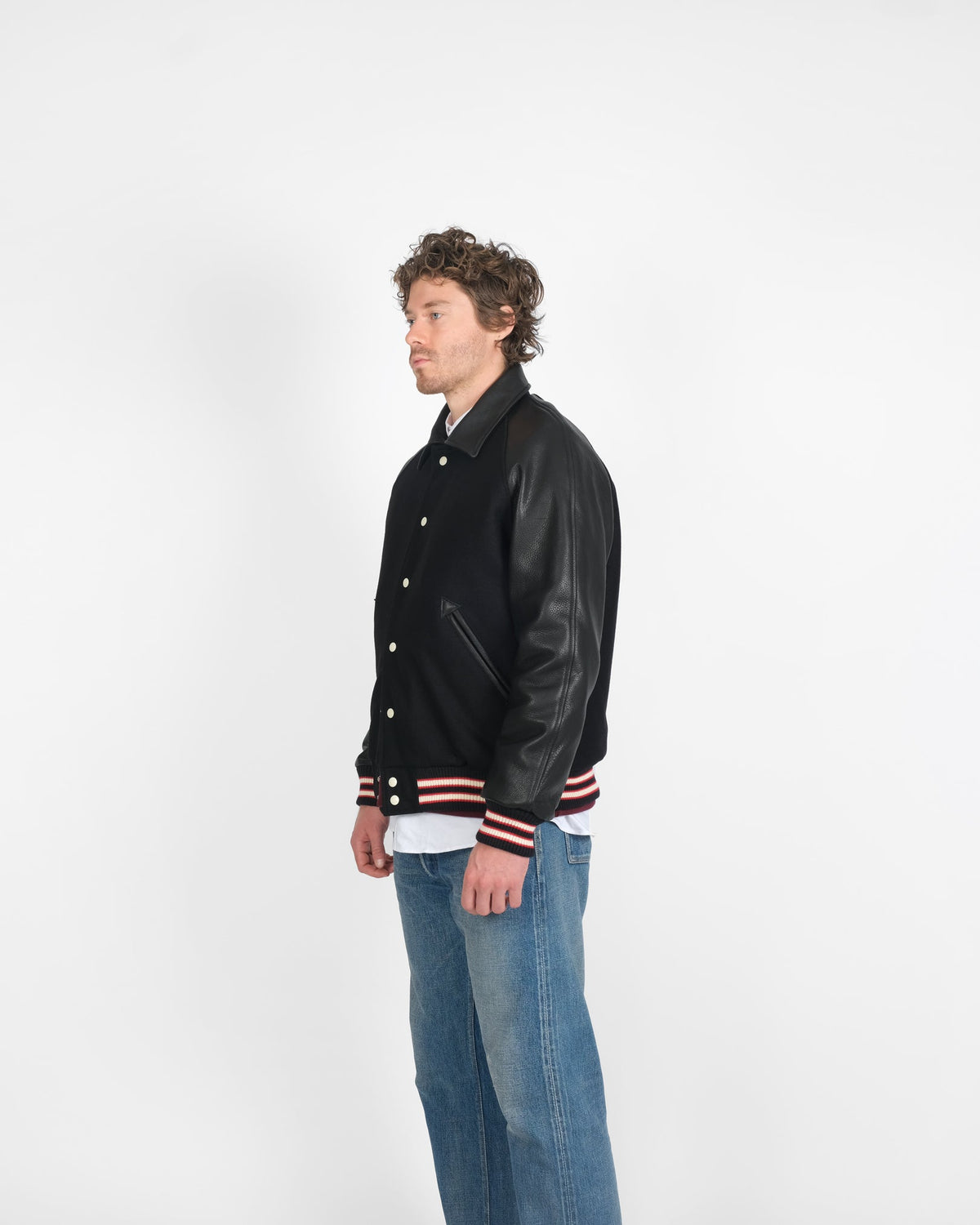 Person wearing a black varsity jacket with leather sleeves on a white background