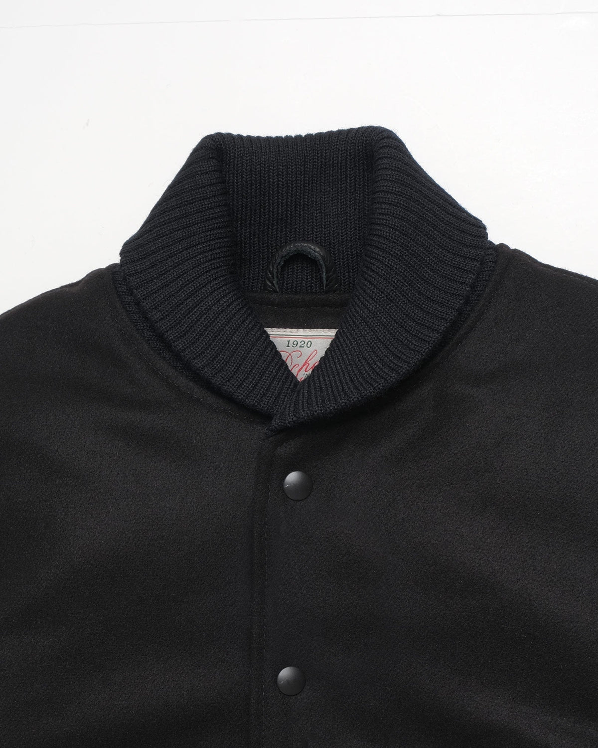 Close-up of a black knit collar and upper front of a varsity-style jacket with snap buttons, on a plain white background.