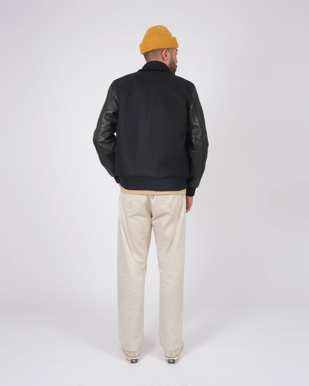 Person wearing a black jacket with leather sleeves and beige pants on a white background