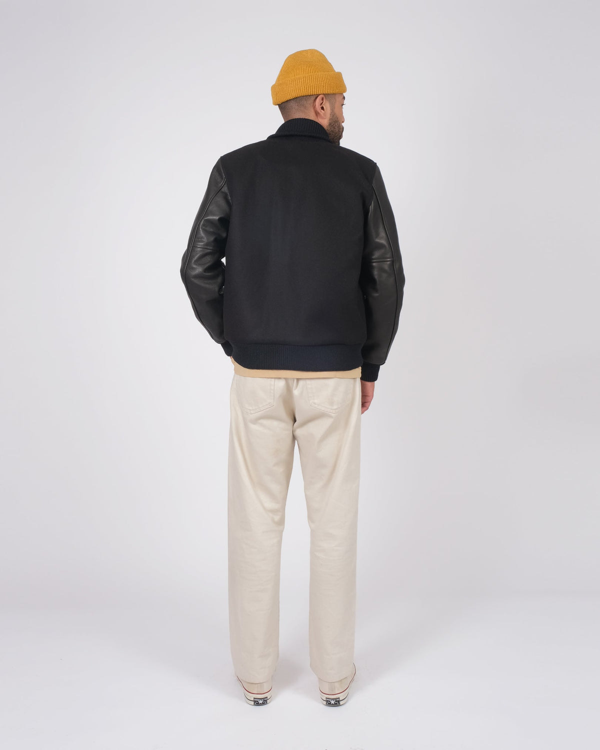 Person wearing a black jacket with leather sleeves and beige pants on a white background