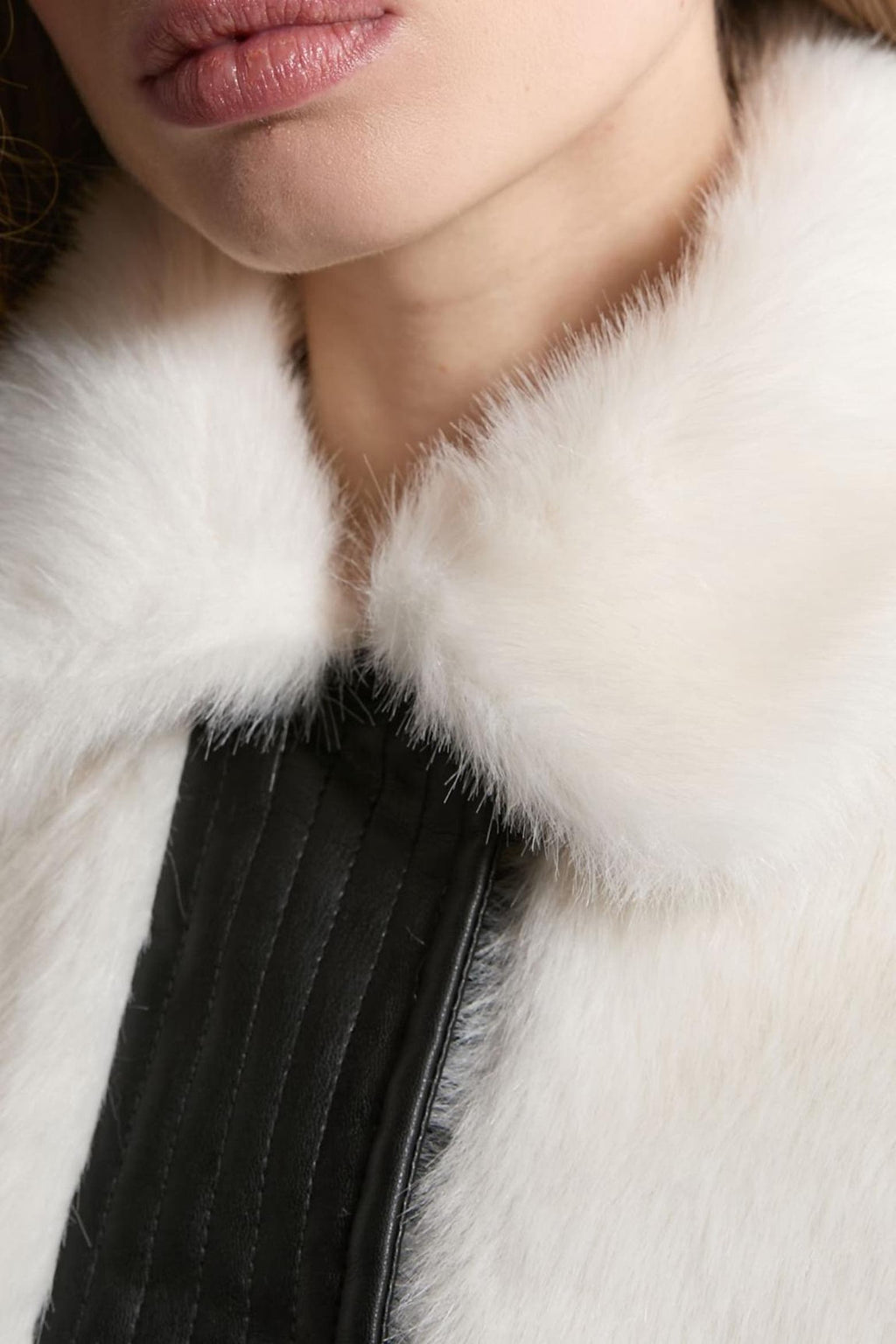 Close-up of a model wearing a luxurious white fur collar with a black quilted leather panel.