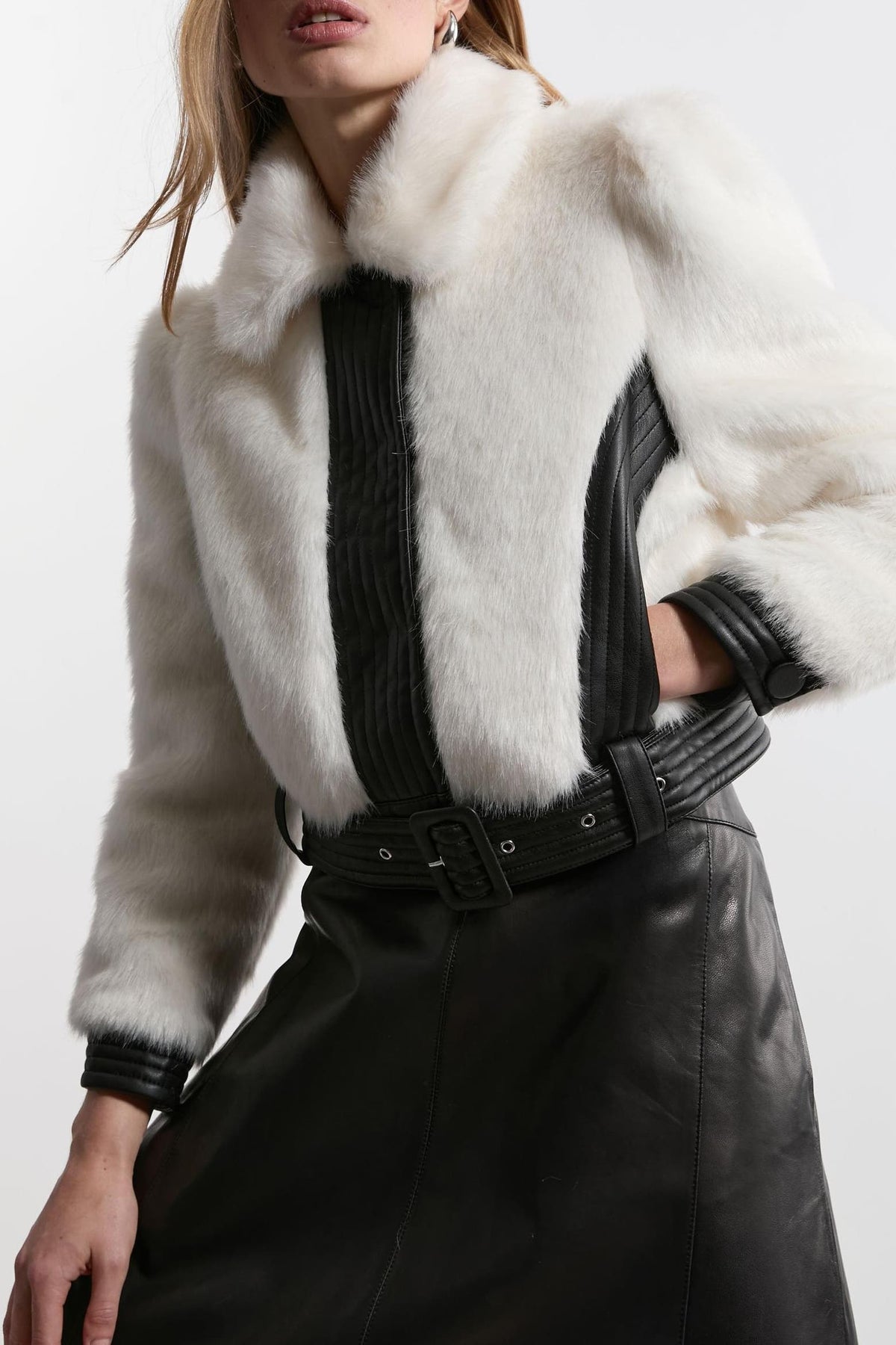 A close-up of a model wearing a white faux jacket with black ribbed side panels and a black belt, paired with a black leather skirt.