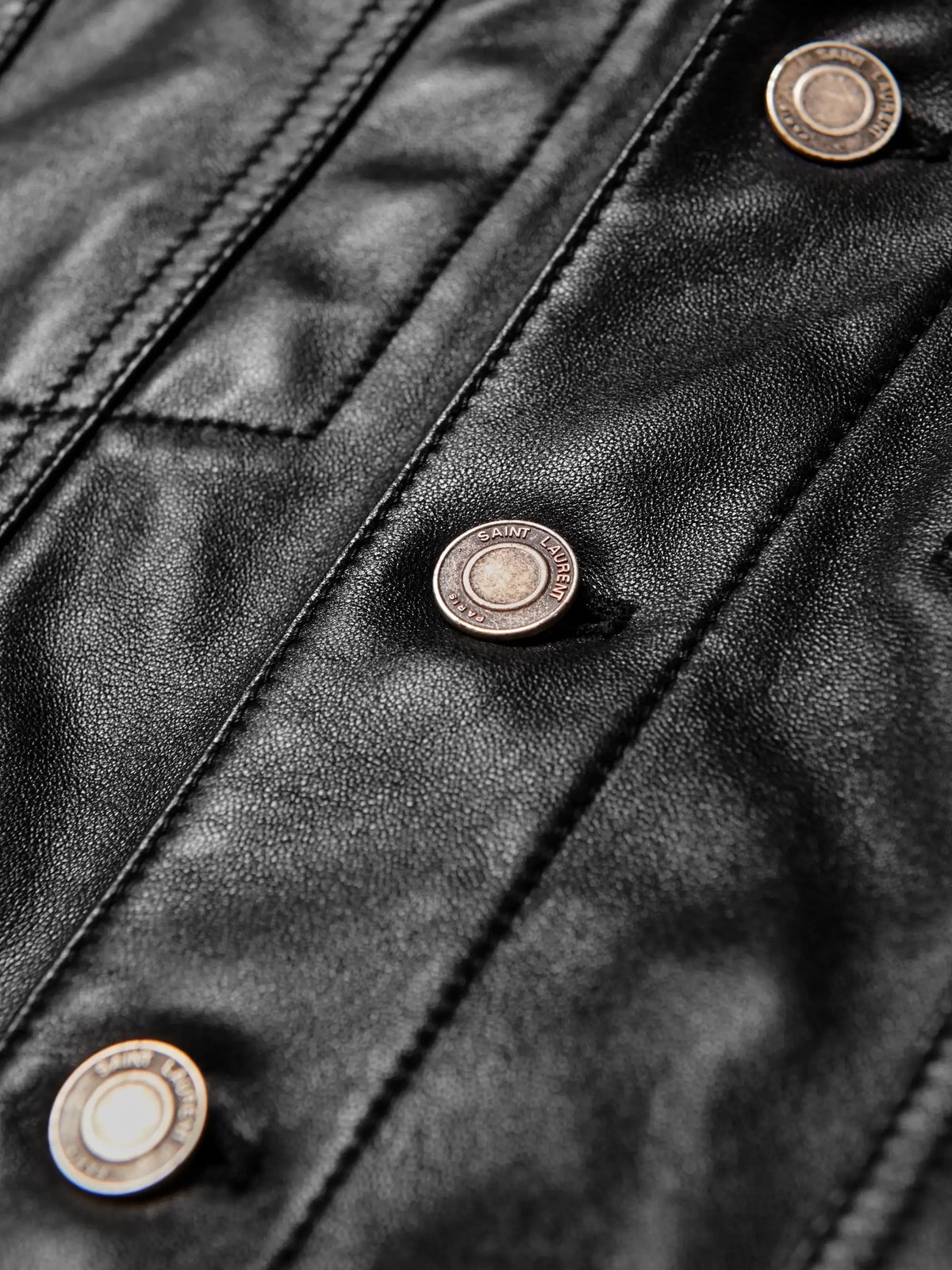 Close-up of a black leather jacket featuring a diagonal button placket with metallic gun-shaped buttons.