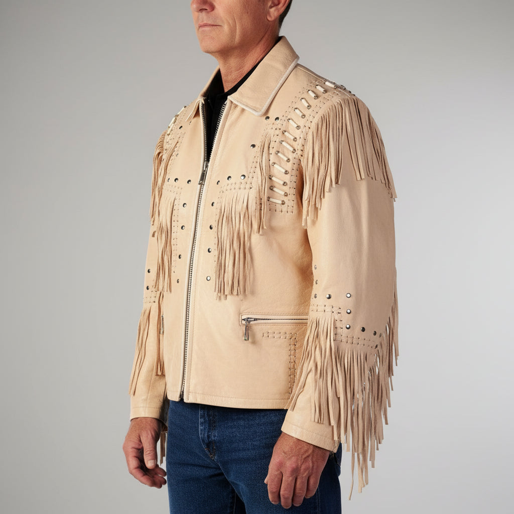 A man wearing a light beige suede fringe jacket with silver studs and a black shirt underneath, paired with blue jeans, photographed against a neutral gray background.