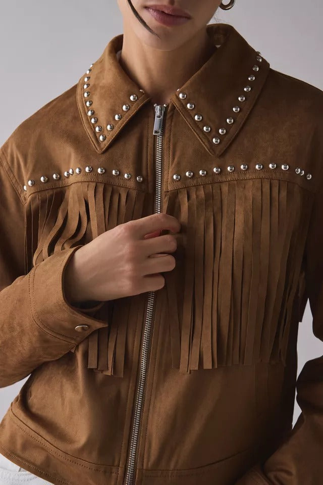 A close-up of a person wearing a brown suede jacket with silver studs and fringe detailing, holding the front zipper.