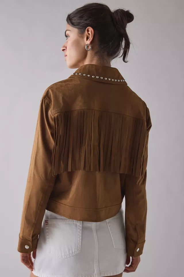 A woman shown from the back wearing a brown suede fringe jacket with silver studs along the collar, paired with a white denim skirt, against a light gray studio background.