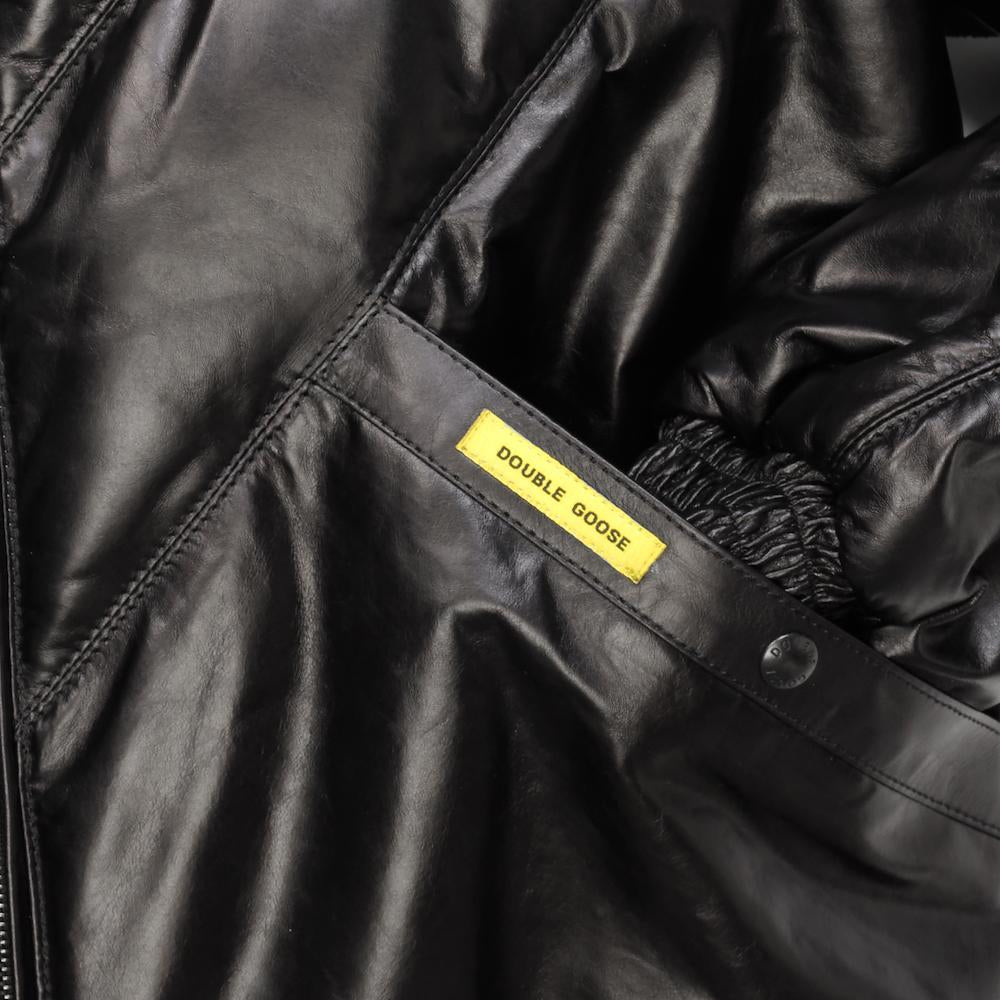 Close-up of a black leather jacket with a yellow brand label reading 'DOUBLE GOOSE' sewn onto the pocket area.
