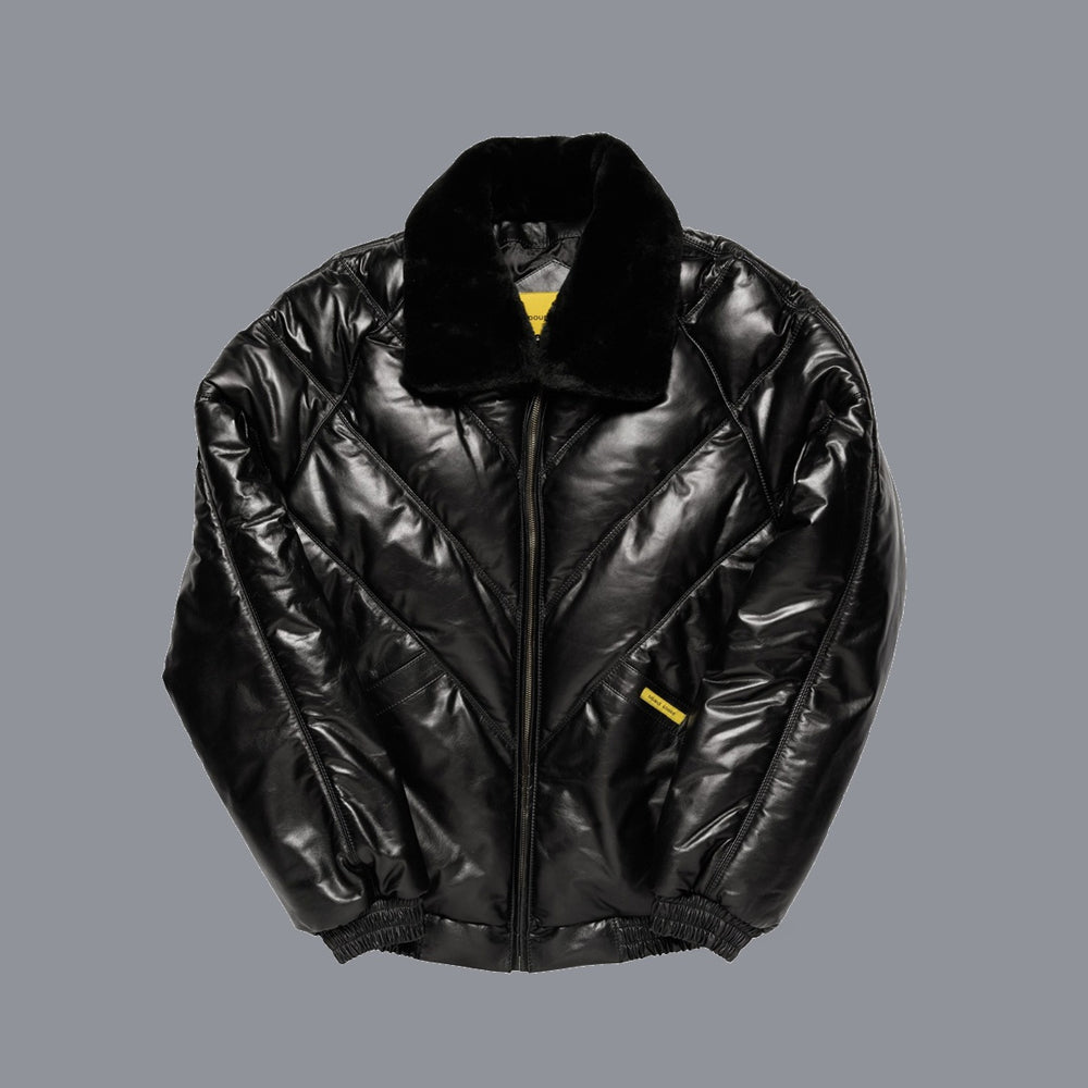 A black V bomber leather jacket with a plush black fur collar, shown flat against a solid gray background. It features a front zipper, elasticized ribbed cuffs and hem, and small yellow accents on the collar interior and a zippered pocket.