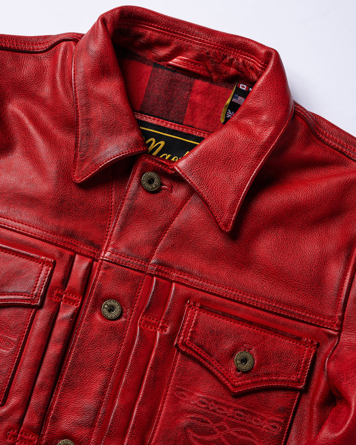 A close-up of a red leather jacket with a pointed collar, dark metal snap buttons, and a red-and-black plaid lining visible inside the collar.