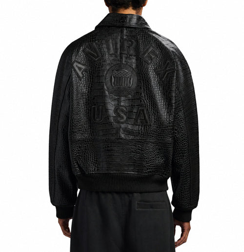 A person shown from the back wearing a black textured leather jacket with a large embossed logo reading 'AURELUX USA' across the back, paired with black pants, on a plain white studio background.