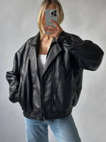 a women wearing a black vintage leather jacket posing in front of mirror holding iphone