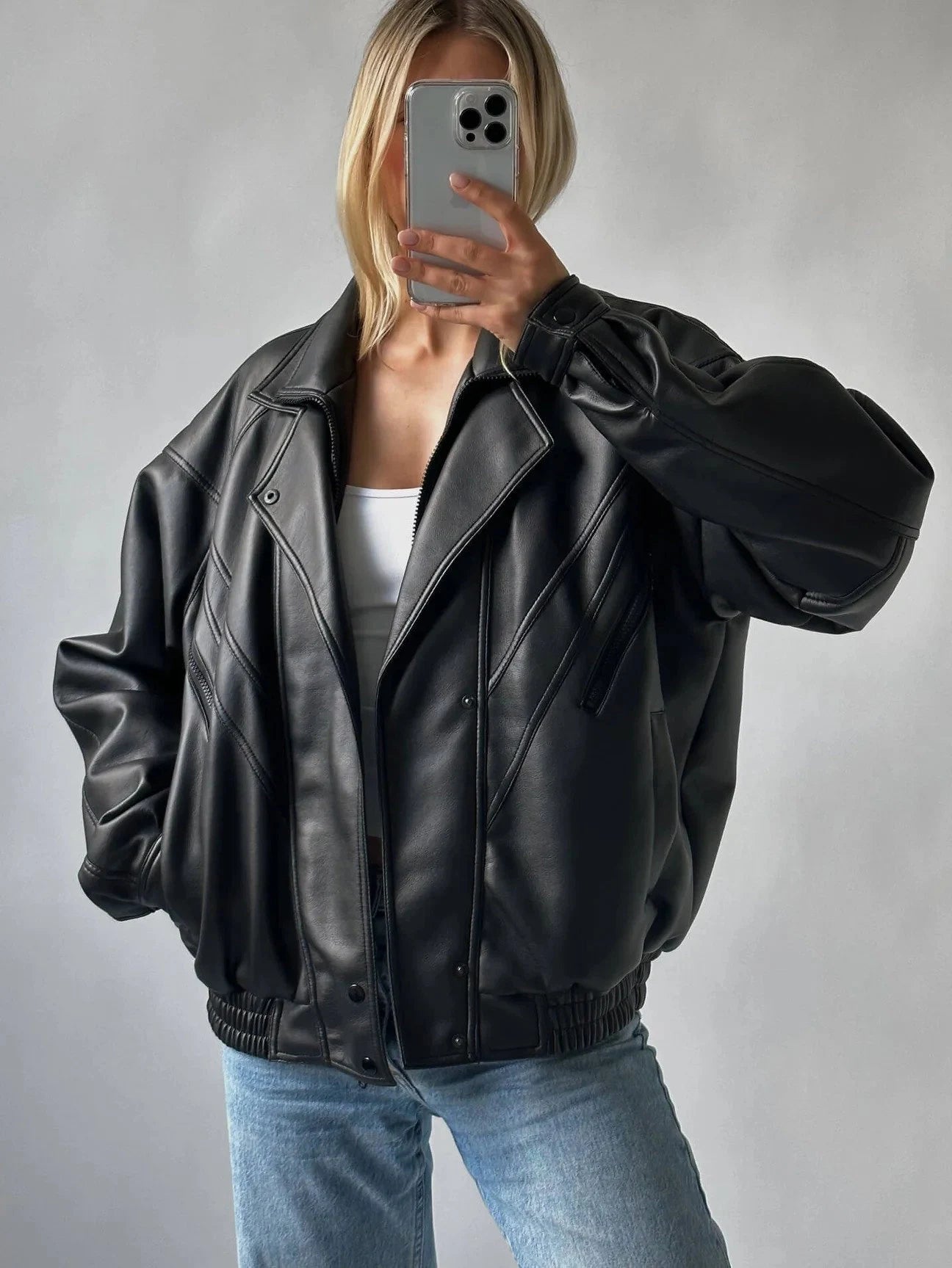 a women wearing a black vintage leather jacket posing in front of mirror holding iphone