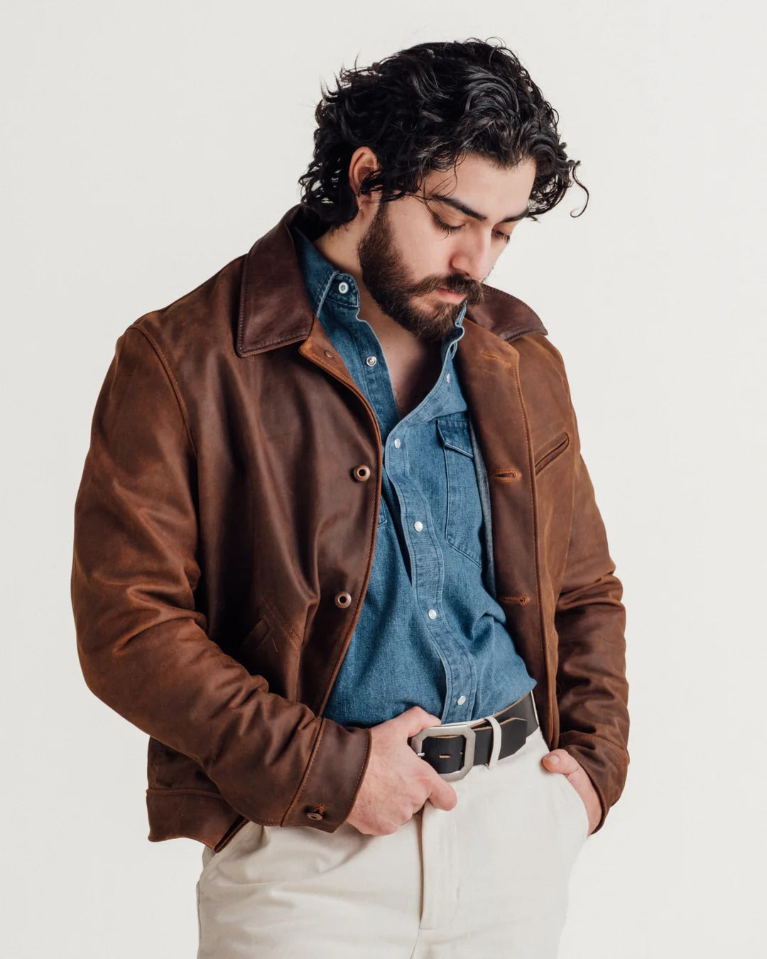 Man wearing a brown leather jacket over a blue shirt with a white background