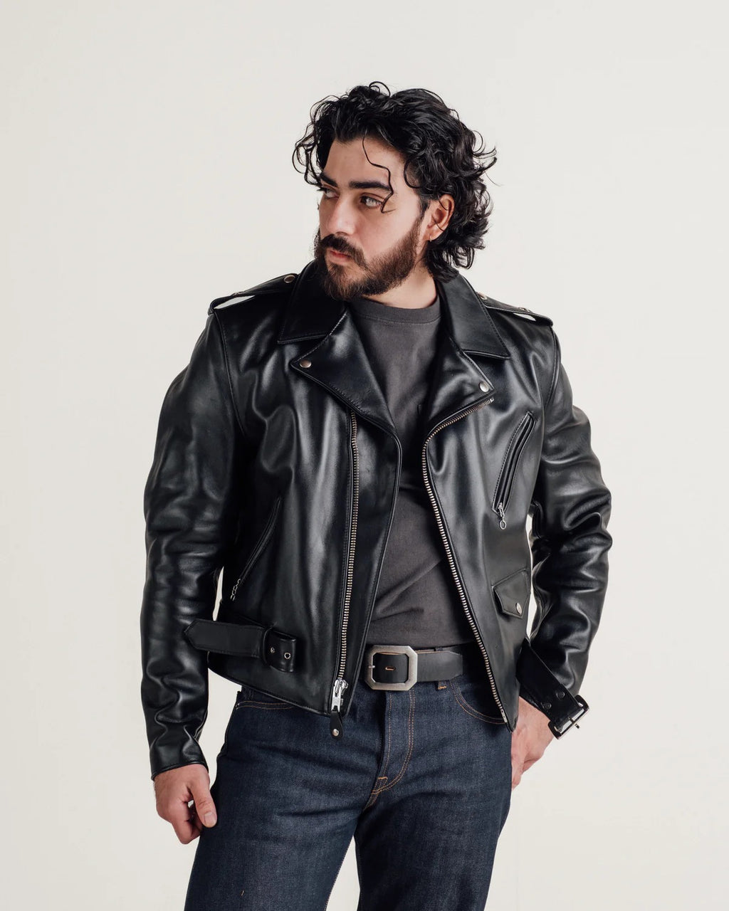Man wearing a black leather jacket and jeans on a light gray background
