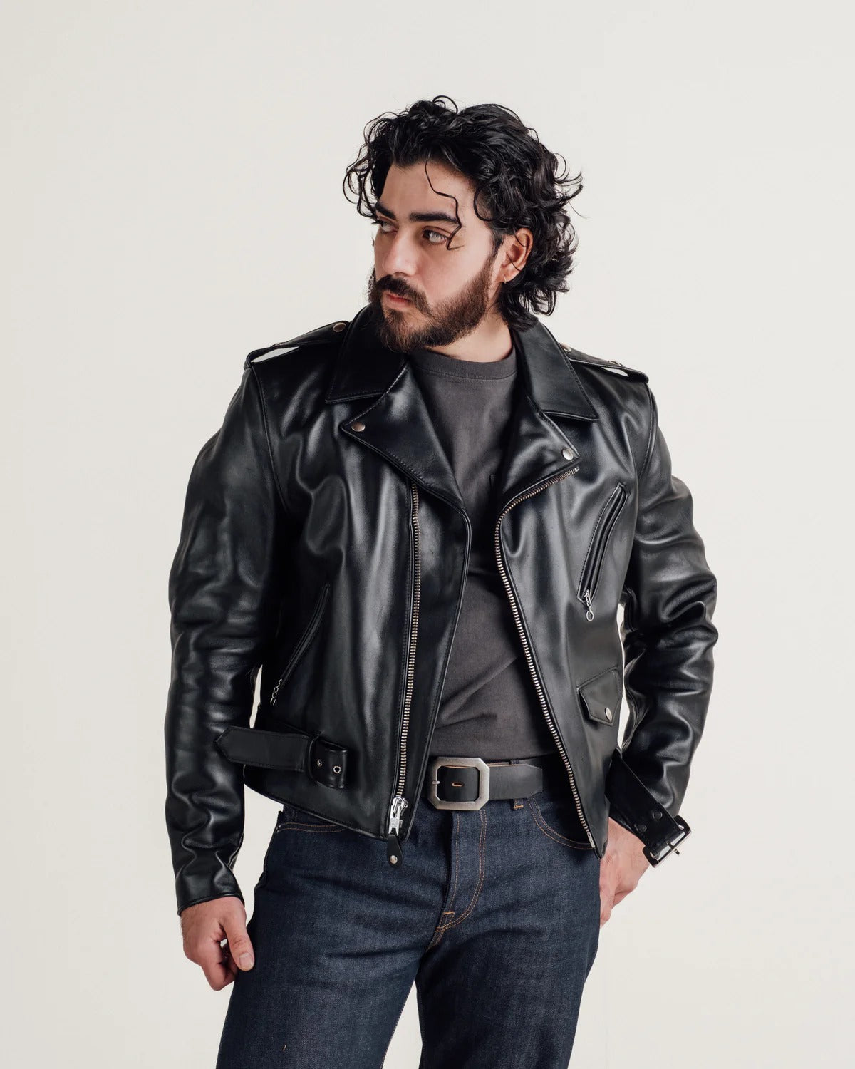 Man wearing a black leather jacket and jeans on a light gray background