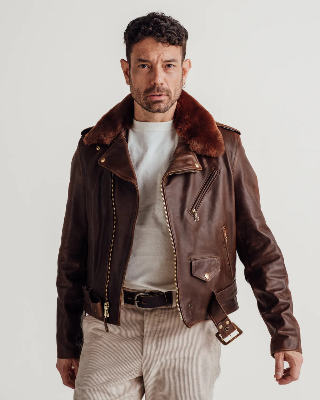 Man wearing a brown leather jacket with fur collar on a white background