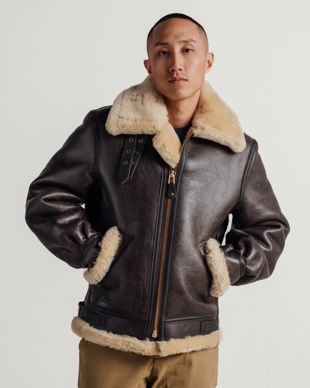 Man wearing a brown leather jacket with fur trim on a white background