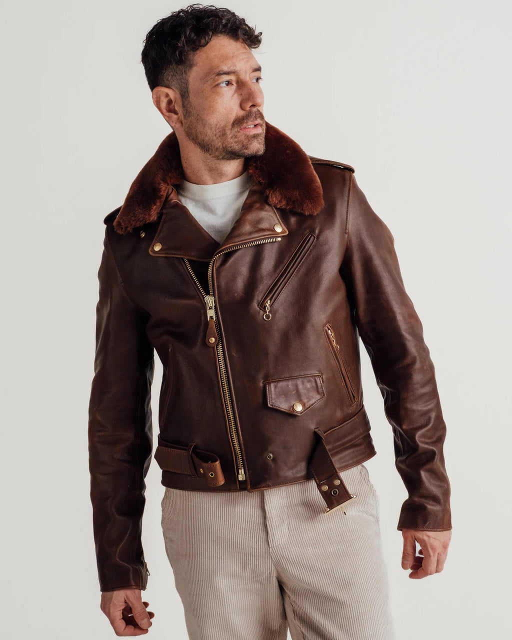 Man wearing a brown leather jacket with fur collar on a light gray background