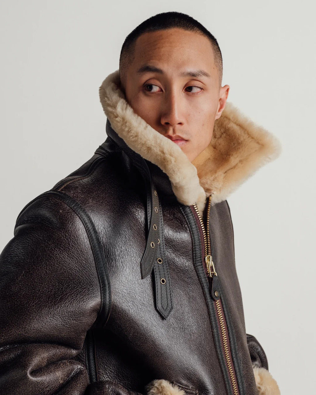 Man wearing a leather jacket with fur collar on a plain background