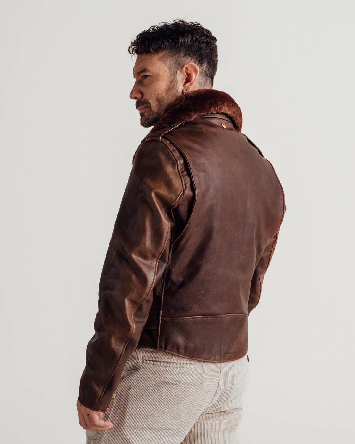 Man wearing a brown leather jacket with fur collar on a plain background