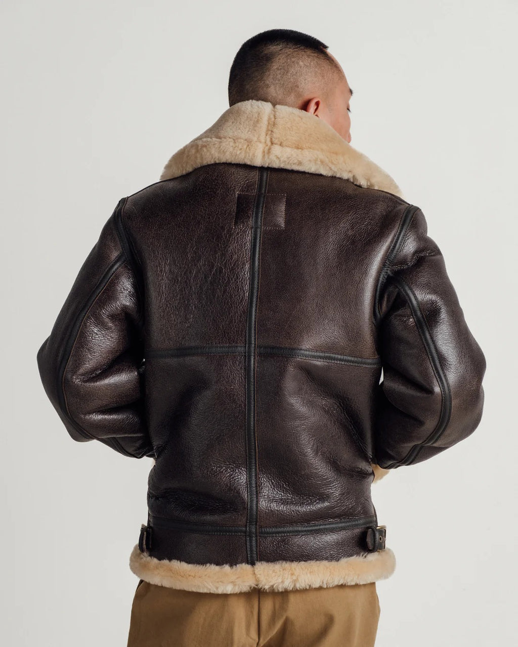 Person wearing a brown leather jacket with fur lining on a plain background