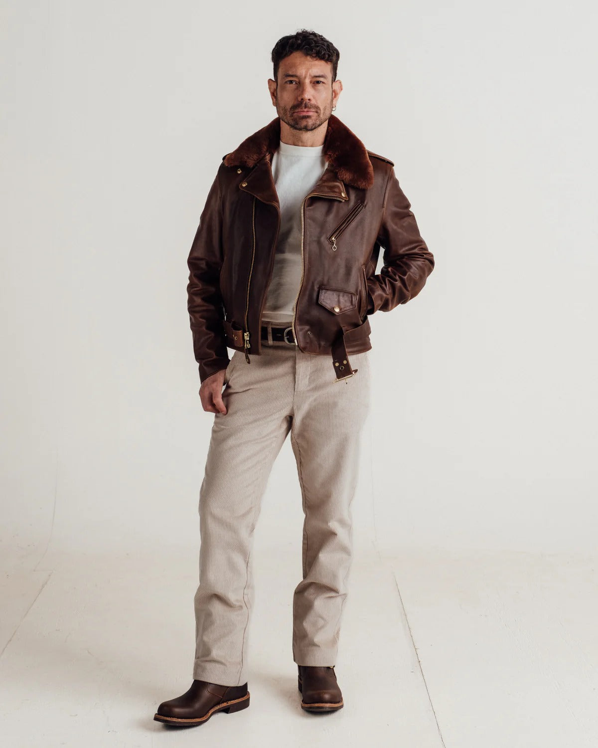 Man wearing a brown leather jacket and beige pants on a white background