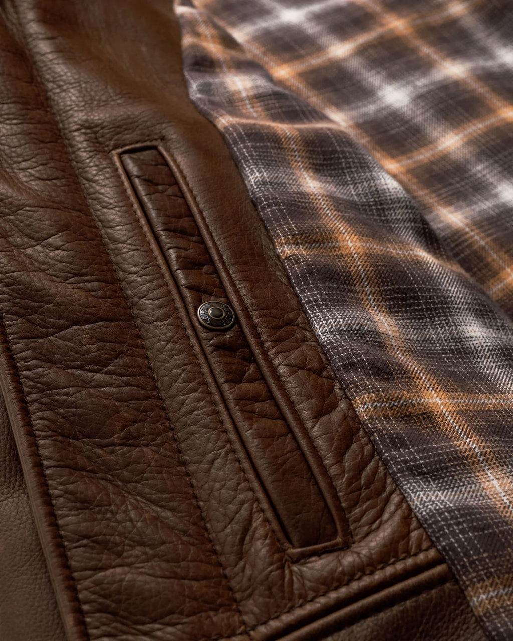 Close-up of a brown leather jacket with a plaid patterned lining.