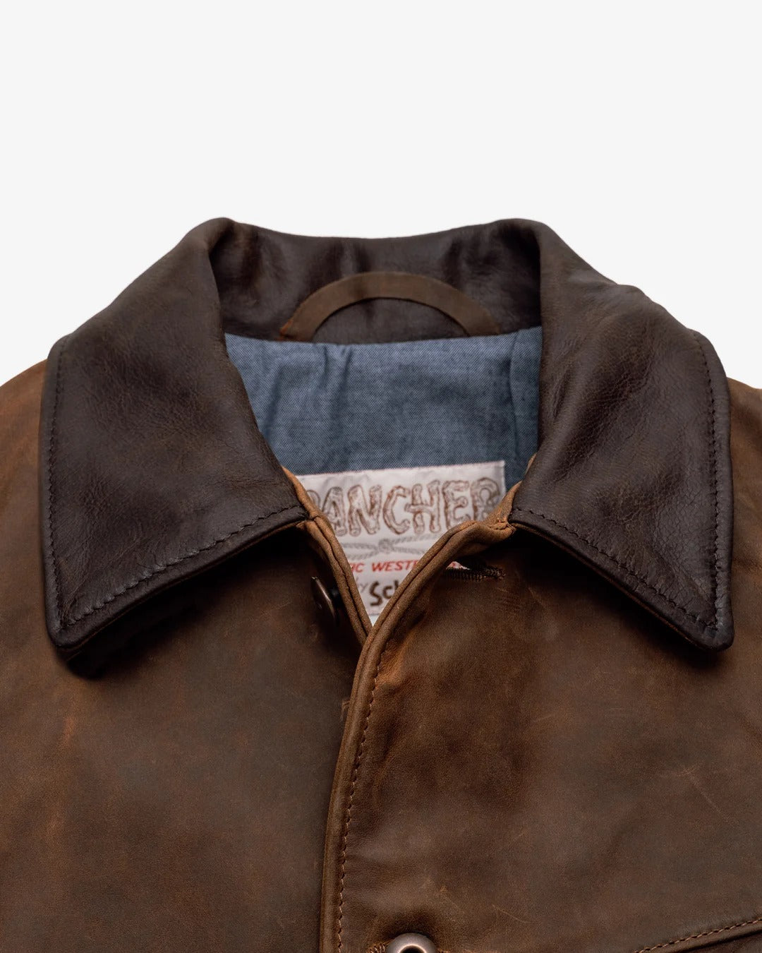 Close-up of a brown leather jacket with a visible brand label on a white background