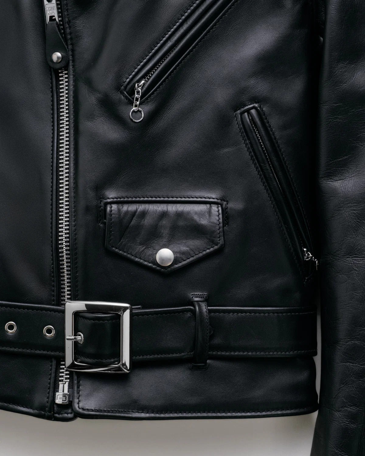 Close-up of a black leather jacket with zipper and belt details.