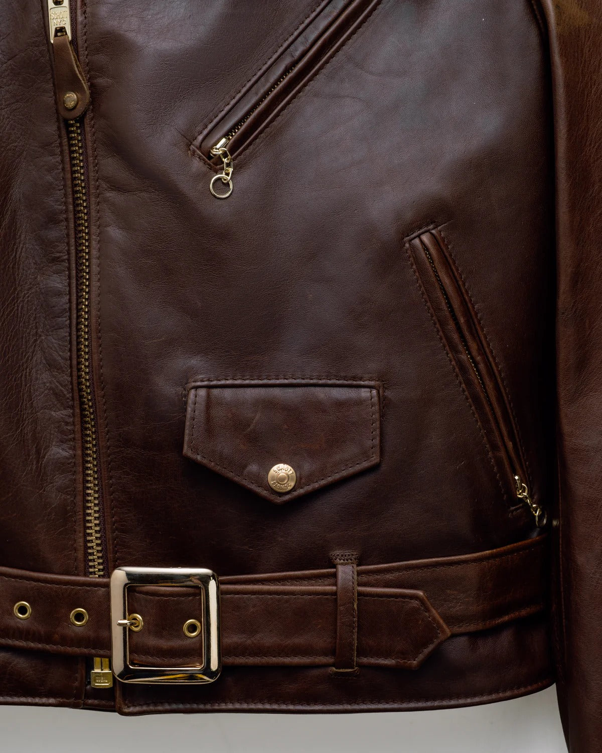 Close-up of a brown leather jacket with zipper and belt buckle on a light gray background
