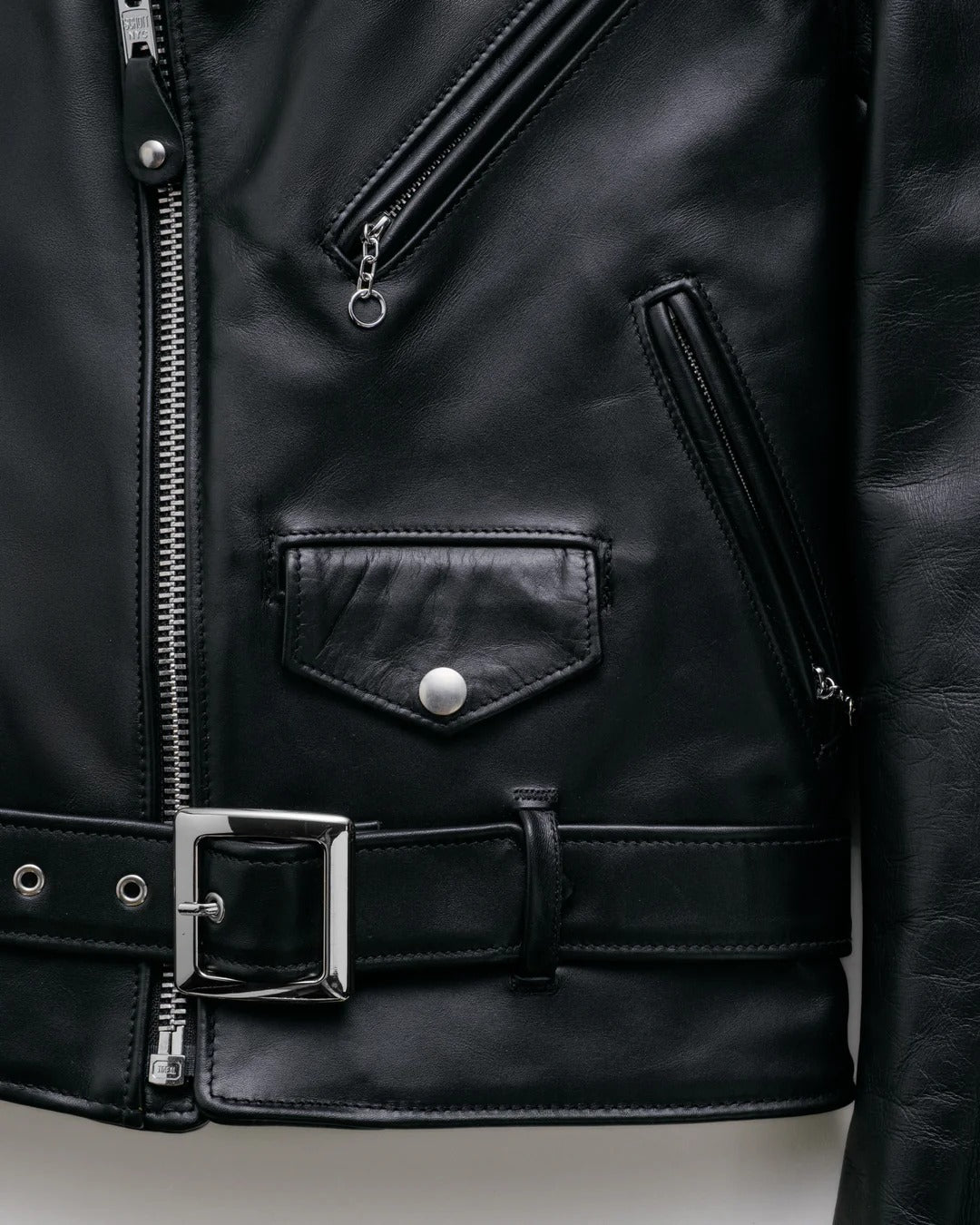 Close-up of a black leather jacket with zipper and buckle details.
