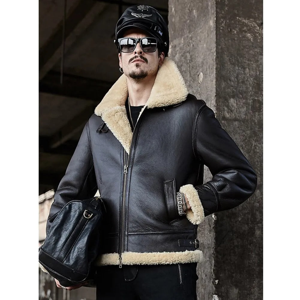 Man wearing a black leather jacket with shearling collar and cuffs, sunglasses, and cap against a dark background.